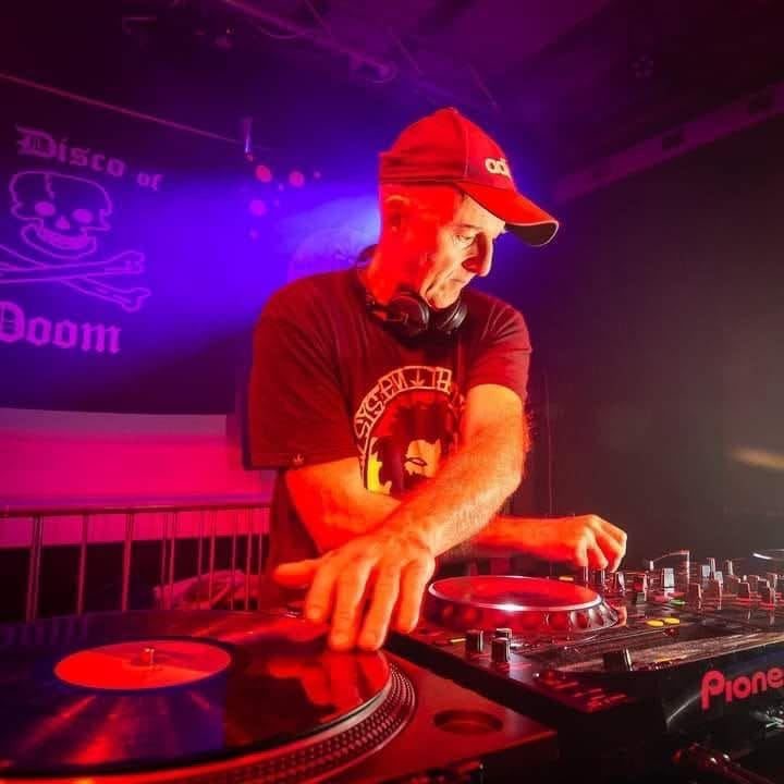 Scragga DJing on Pioneer decks and turntables under red stage light