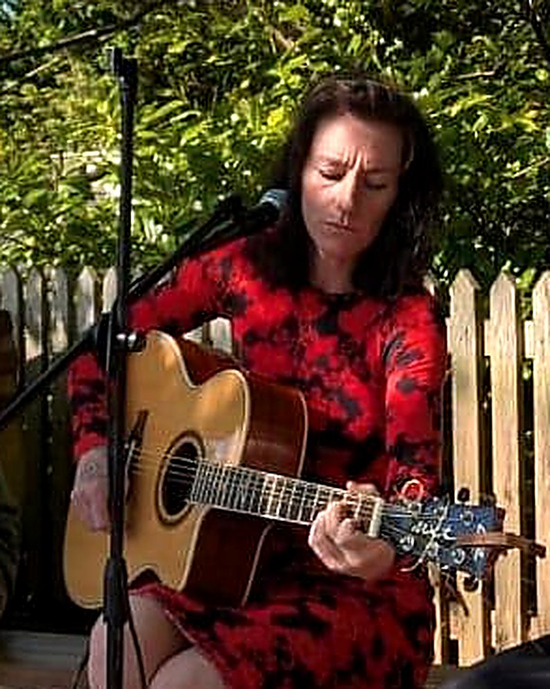 Tallulah Boo Adams playing acoustic guitar and singing outdoors