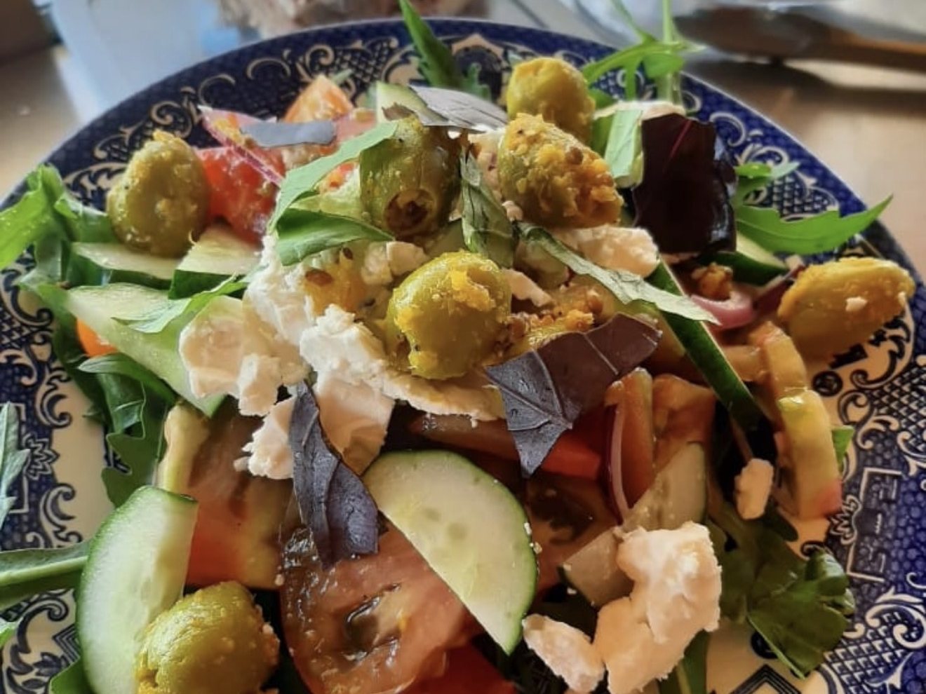 Greek Garden Salad — tomatoes, cucumber, rocket, feta and Moroccan green olives on a blue willow-pattern plate