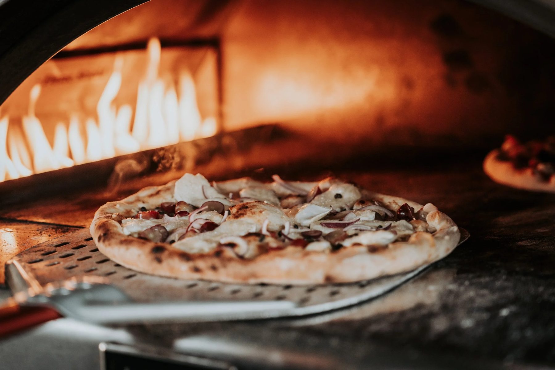 A freshly baked sourdough pizza being lifted from the oven